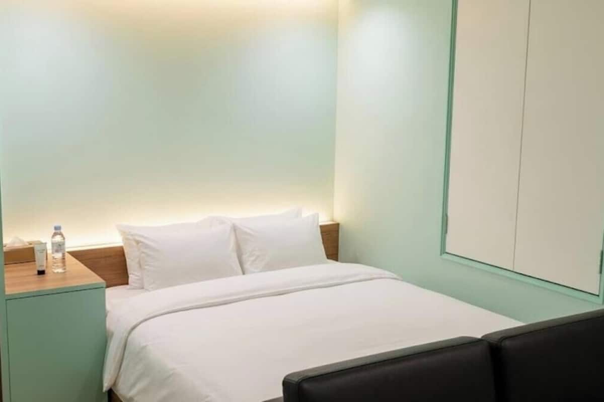Une chambre d’hôtel avec un lit, une table de chevet sur laquelle se trouve une bouteille, et une armoire.