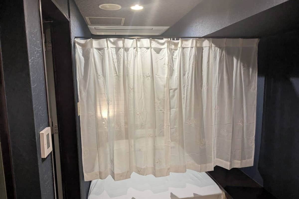 Une petite pièce à la lumière tamisée, avec un lit recouvert d’un fin rideau blanc orné de motifs floraux.