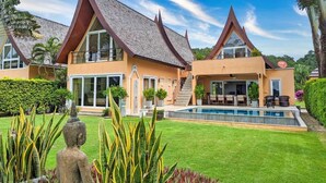 Ein modernes Haus mit Swimmingpool, einem gepflegten Rasen und einer Statue im Vordergrund.
