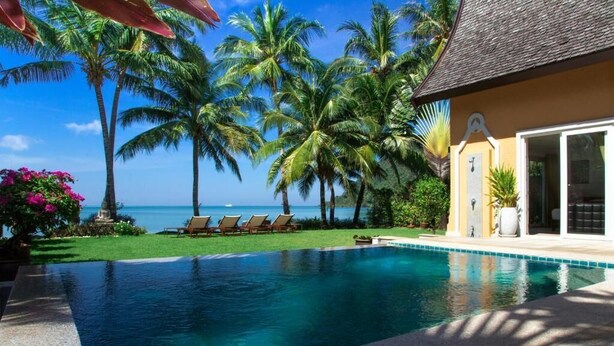 Ein Pool mit Liegestühlen, Palmen und Blick aufs Meer.
