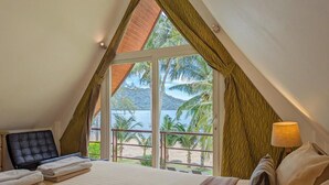 Ein Schlafzimmer mit großem Fenster, einem Bett, einem Sessel und einem Nachttisch mit Lampe.