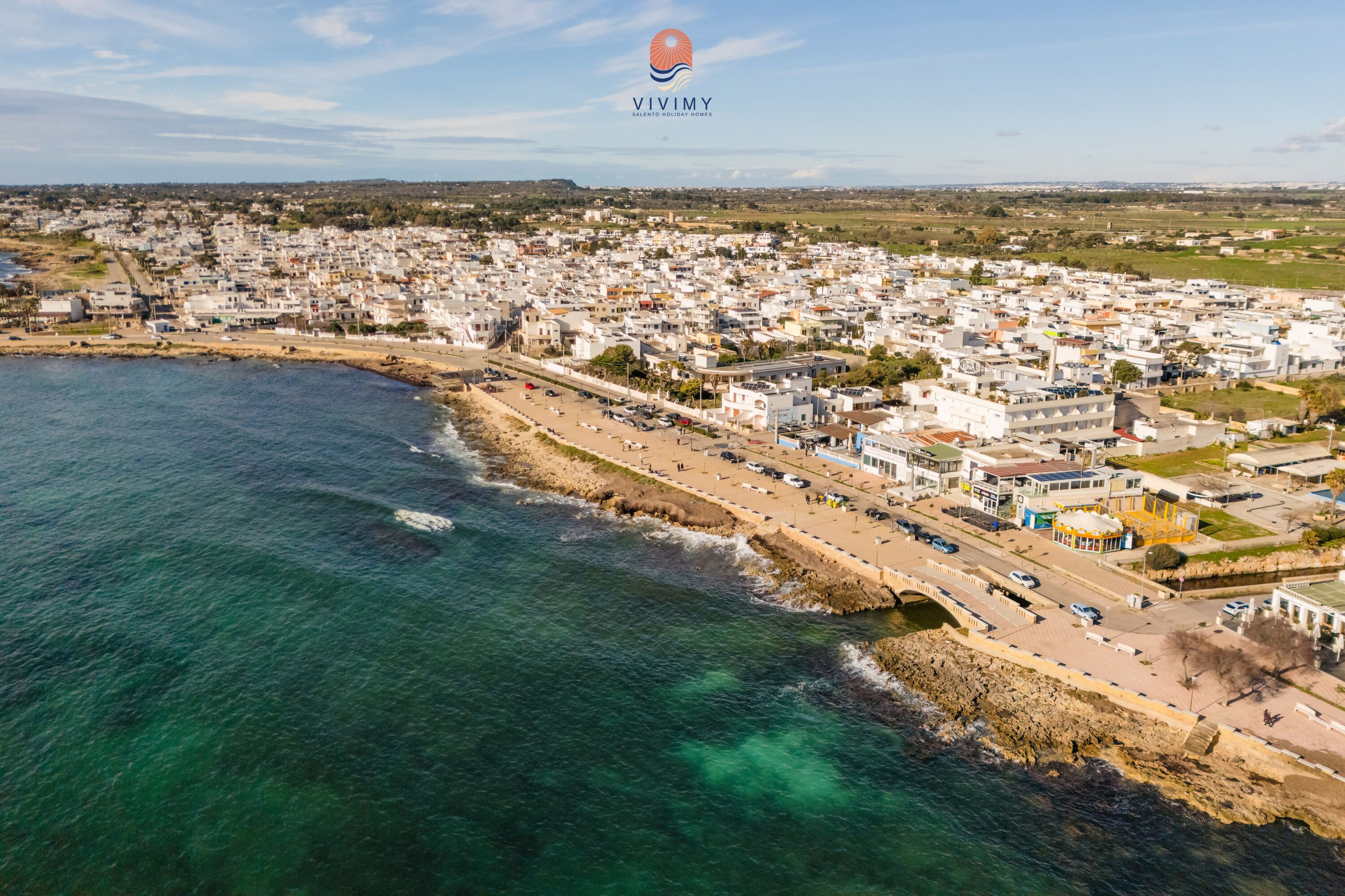 An aerial view of a coastal town with a beach, buildings, and a clear sky.