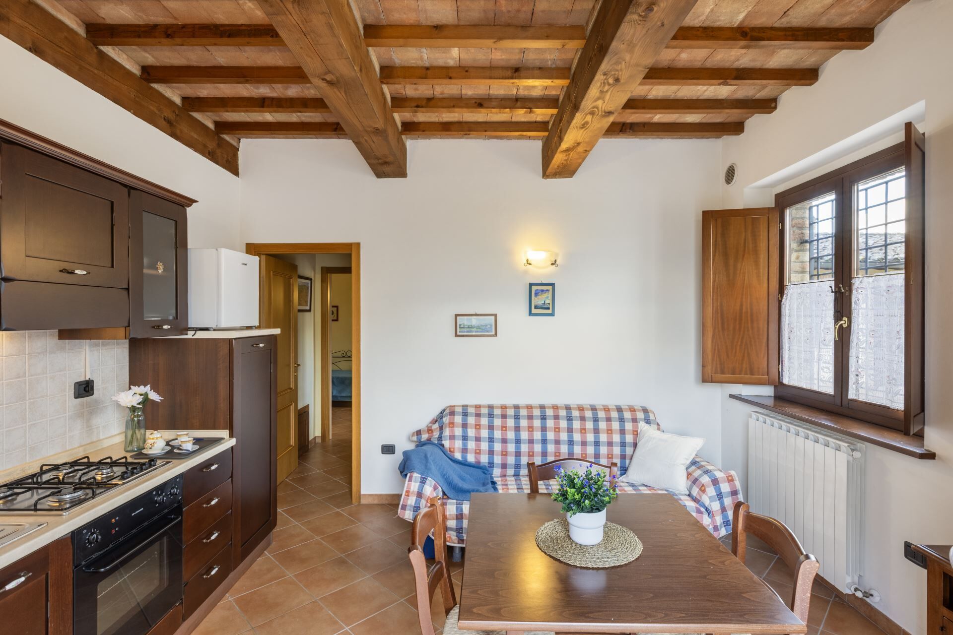 Una cucina funzionale con travi in legno, un'area pranzo con tovaglia a scacchi e vista da una finestra.
