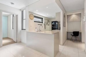 A modern kitchen with a central island, a dining area with a black chair, and a visible door leading to another room. - Open-Plan 2BR Unit w/ Parking in Prime Bondi Beach (Bondi Beach)