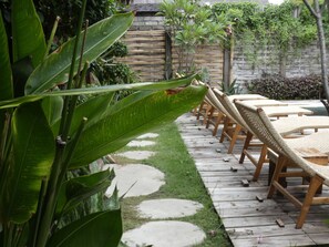 Een tuin met een houten terras, lounge stoelen en een pad van stenen.