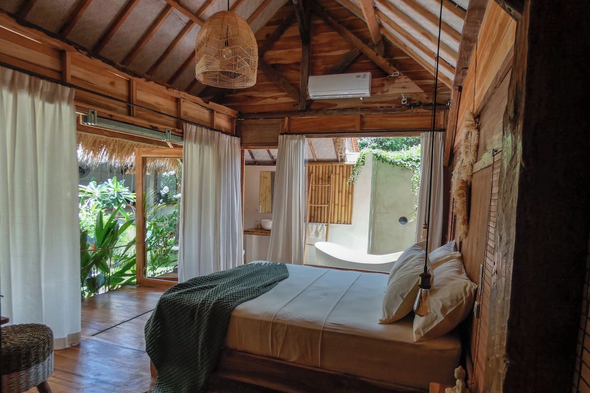Een houten kamer met een bed, een hanglamp en uitzicht op groen buiten.
