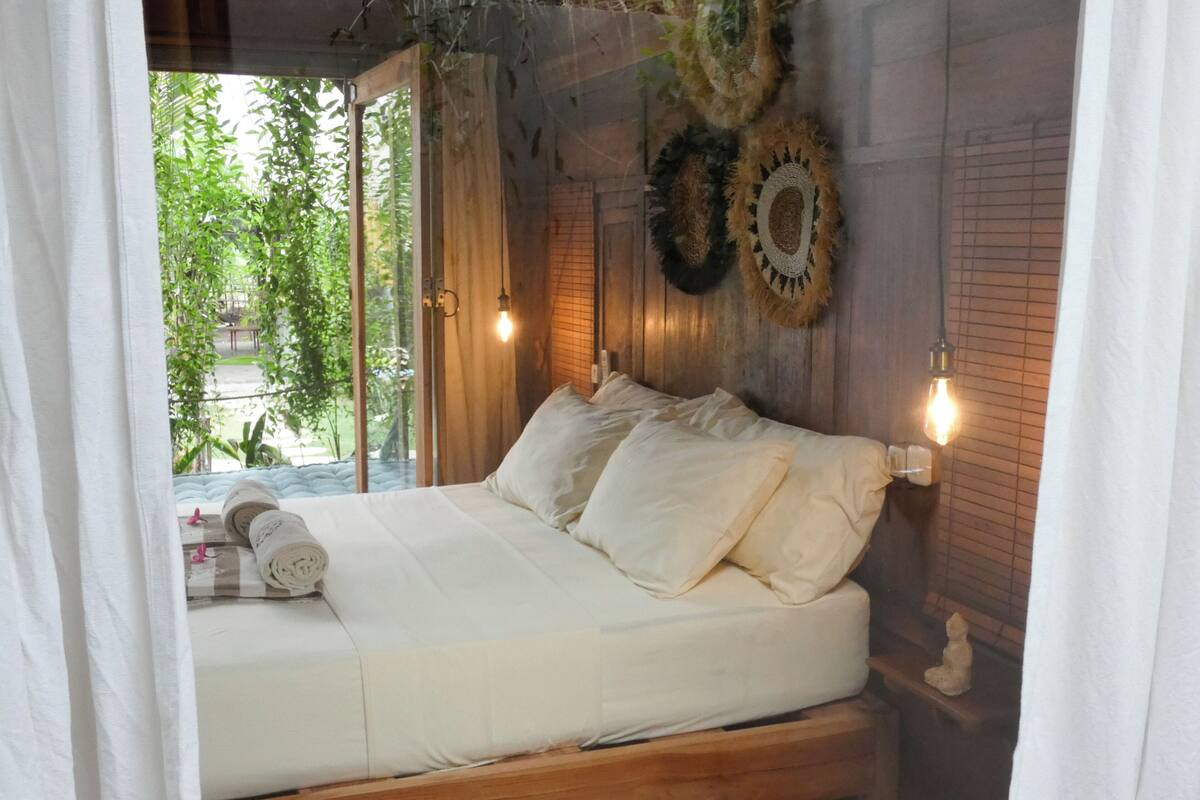 Een bed met witte lakens, een houten hoofdbord en twee wandlampen.