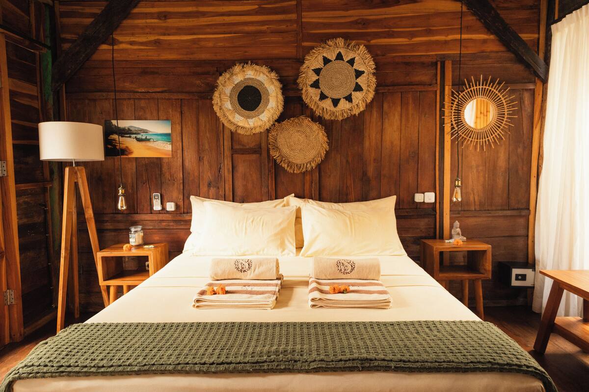 Een houten slaapkamer met een bed, kussens, een lamp en decoratie aan de muur.