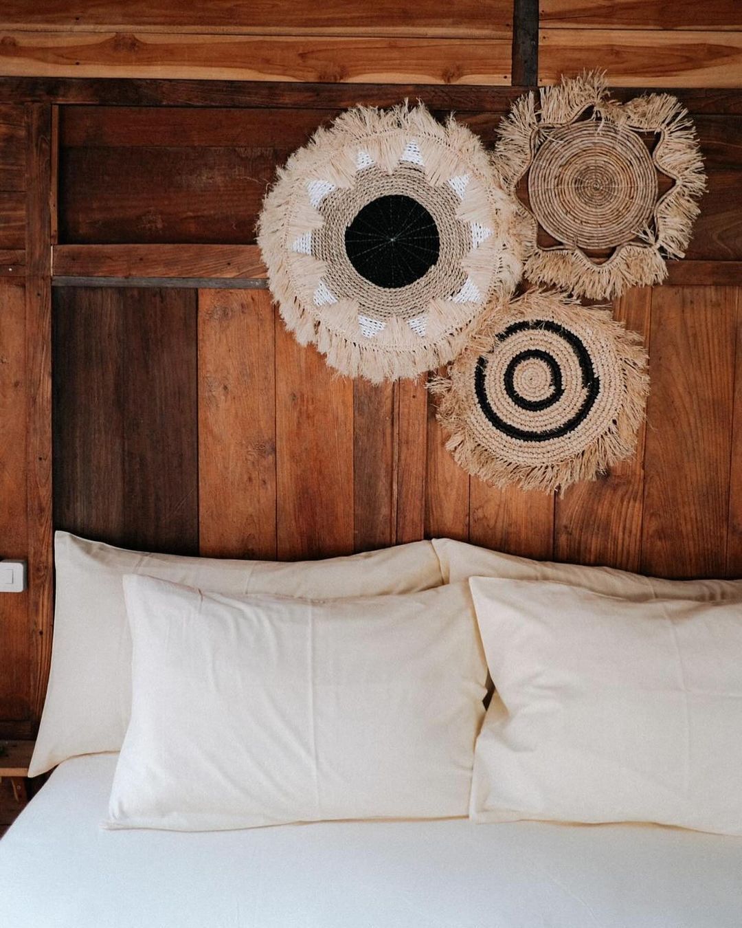 Un lit avec du linge de lit blanc et trois tentures murales tissées aux motifs différents.