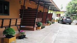 Edifício com escadaria coberta, plantas em vasos e um carro estacionado.