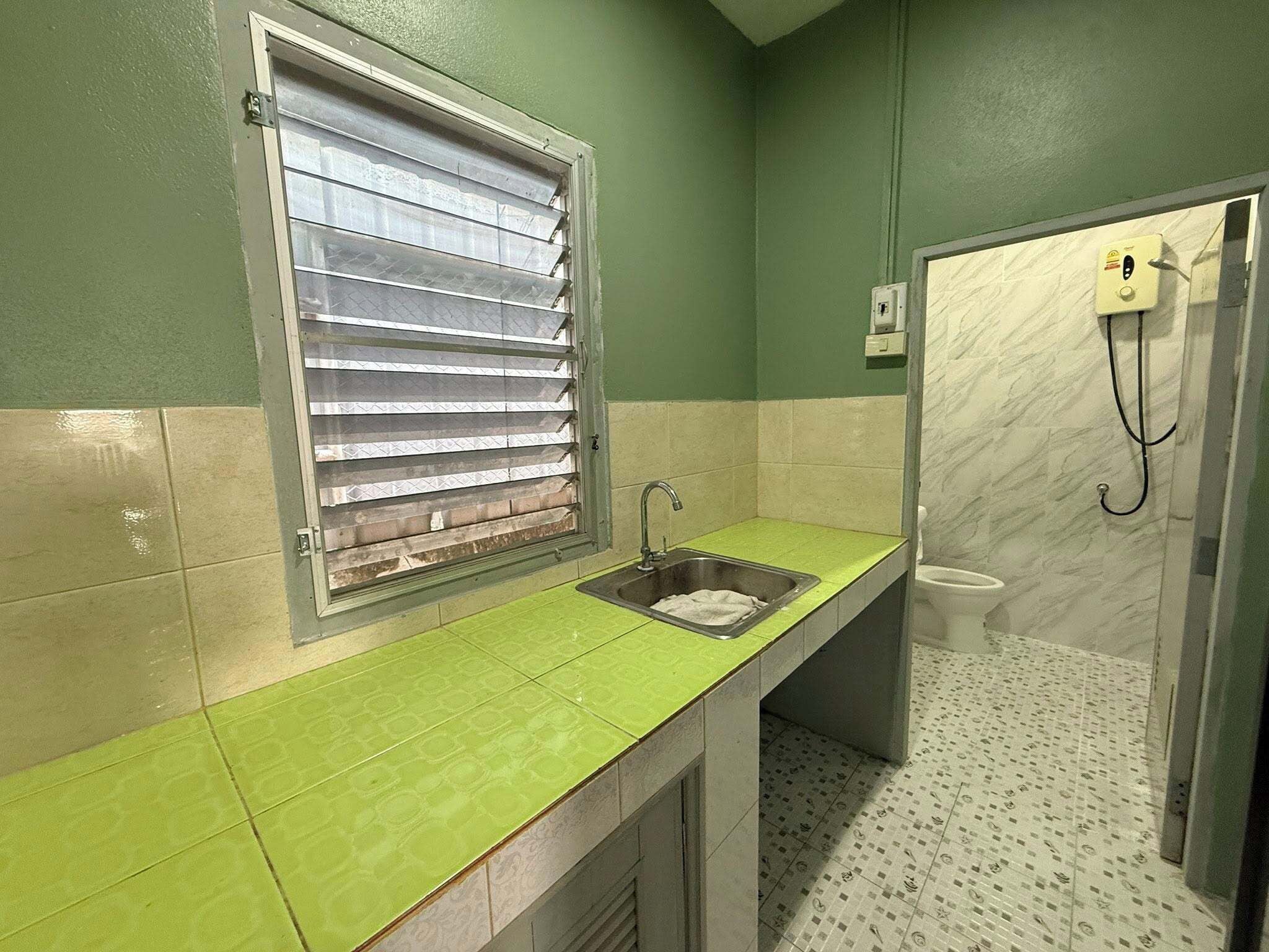 A bathroom with a green countertop, a window with blinds, a toilet, and a shower area.
