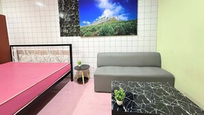 Quarto pequeno e moderno com uma cama, um sofá, uma mesinha com uma planta e um quadro grande na parede.