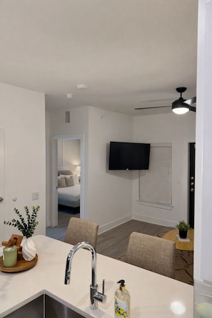 A modern kitchen with a built-in sink, a ceiling fan, and a flat-screen TV mounted on the wall. - Serene City Escape (Frisco)