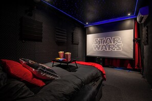 Ein Star Wars-zimmer mit großem Bildschirm, Popcorn und einem Bett mit roter Bettwäsche.