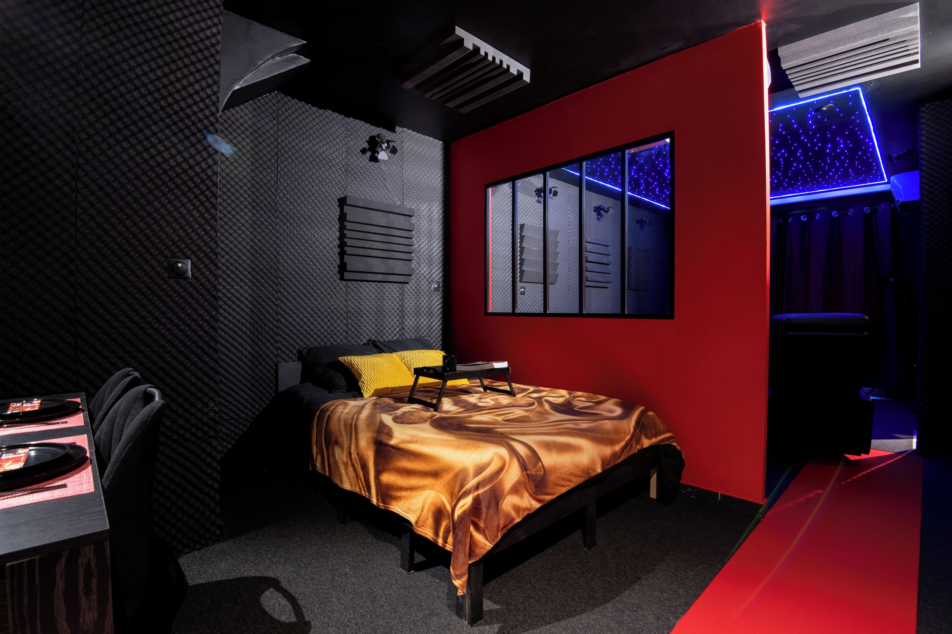 Quarto moderno com cama, escrivaninha com computador e sistema de som fixado na parede.