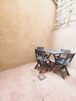 Eine Eckterrasse mit Tisch und Stühlen, einem gefliesten Boden und einer strukturierten Wand.