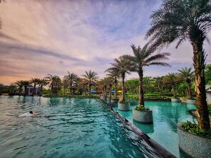 A swimming pool with palm trees and planters, surrounded by greenery. - Nest By SanLiving - 1BR - PIK (Jakarta)