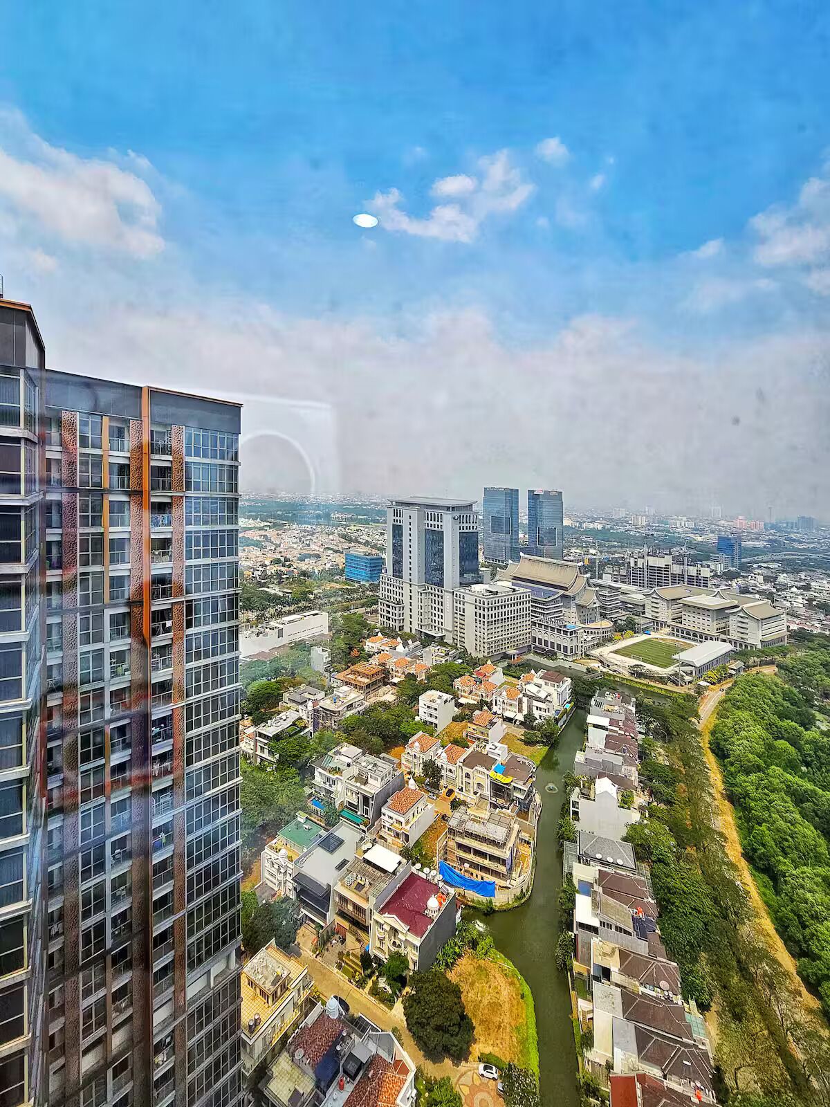 A high-rise building with a modern design, surrounded by a mix of residential and commercial buildings, and a river running through the area.