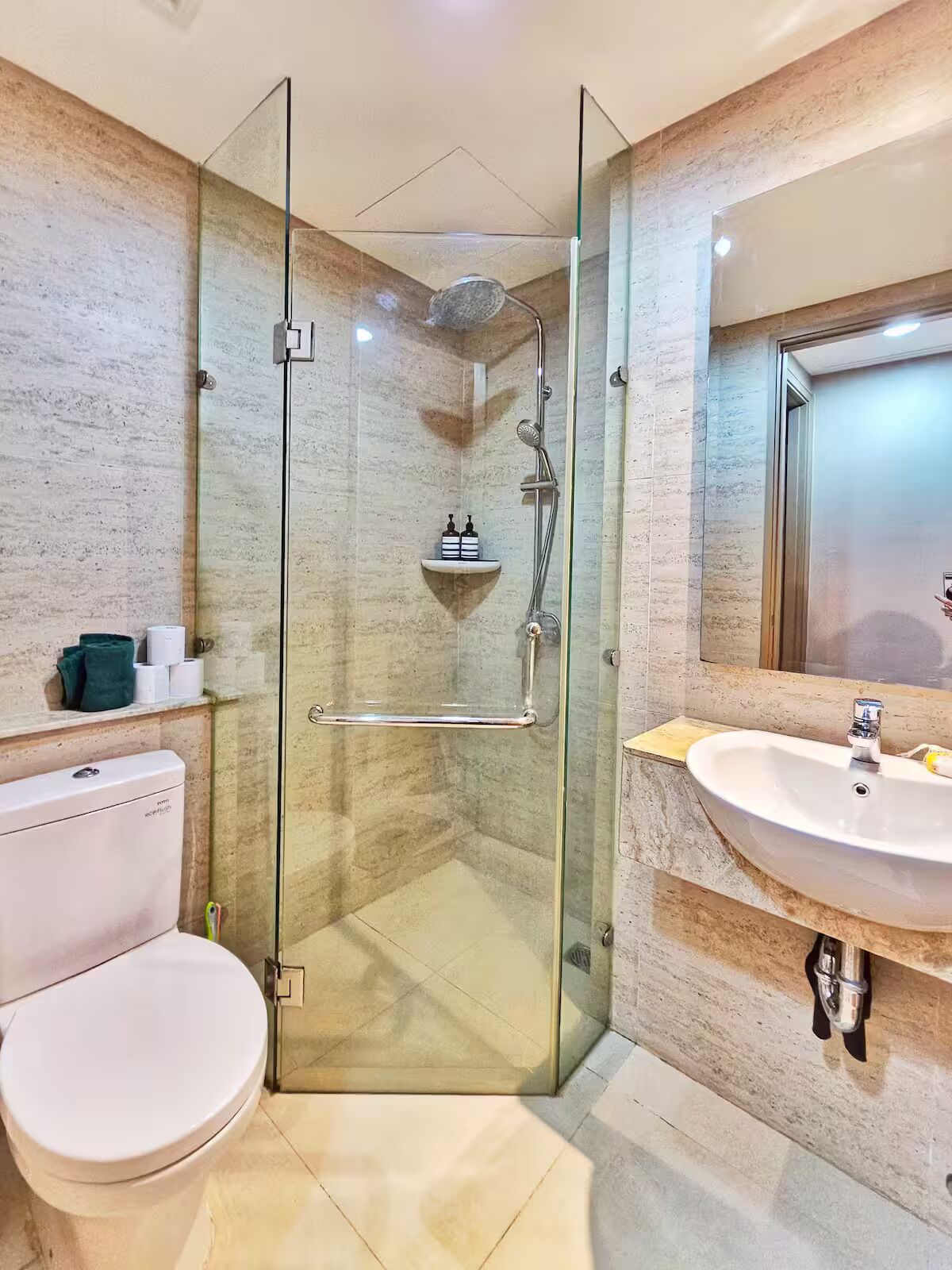 Un baño moderno con ducha acristalada, inodoro blanco y lavamanos con espejo.