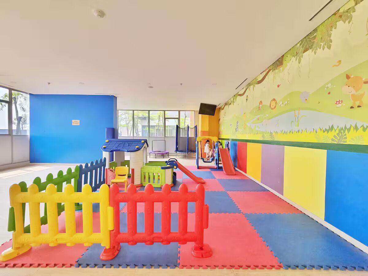 Espaço infantil com tapetes coloridos, escorrega e estrutura de escalada.