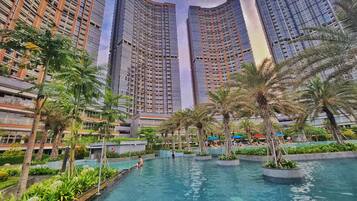 A modern hotel with a large outdoor swimming pool surrounded by palm trees and greenery.