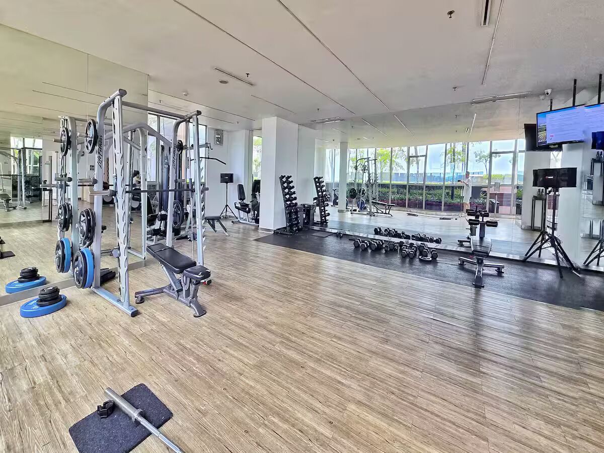 Une salle de sport spacieuse, équipée de divers appareils d’exercice, dotée de grandes fenêtres et d’un téléviseur à écran plat.