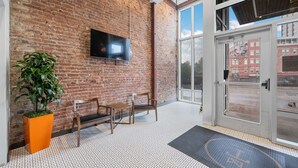 Un espace d’accueil avec un mur en briques, un téléviseur à écran plat, deux chaises en bois, une plante en pot et une porte en verre donnant sur l’extérieur.
