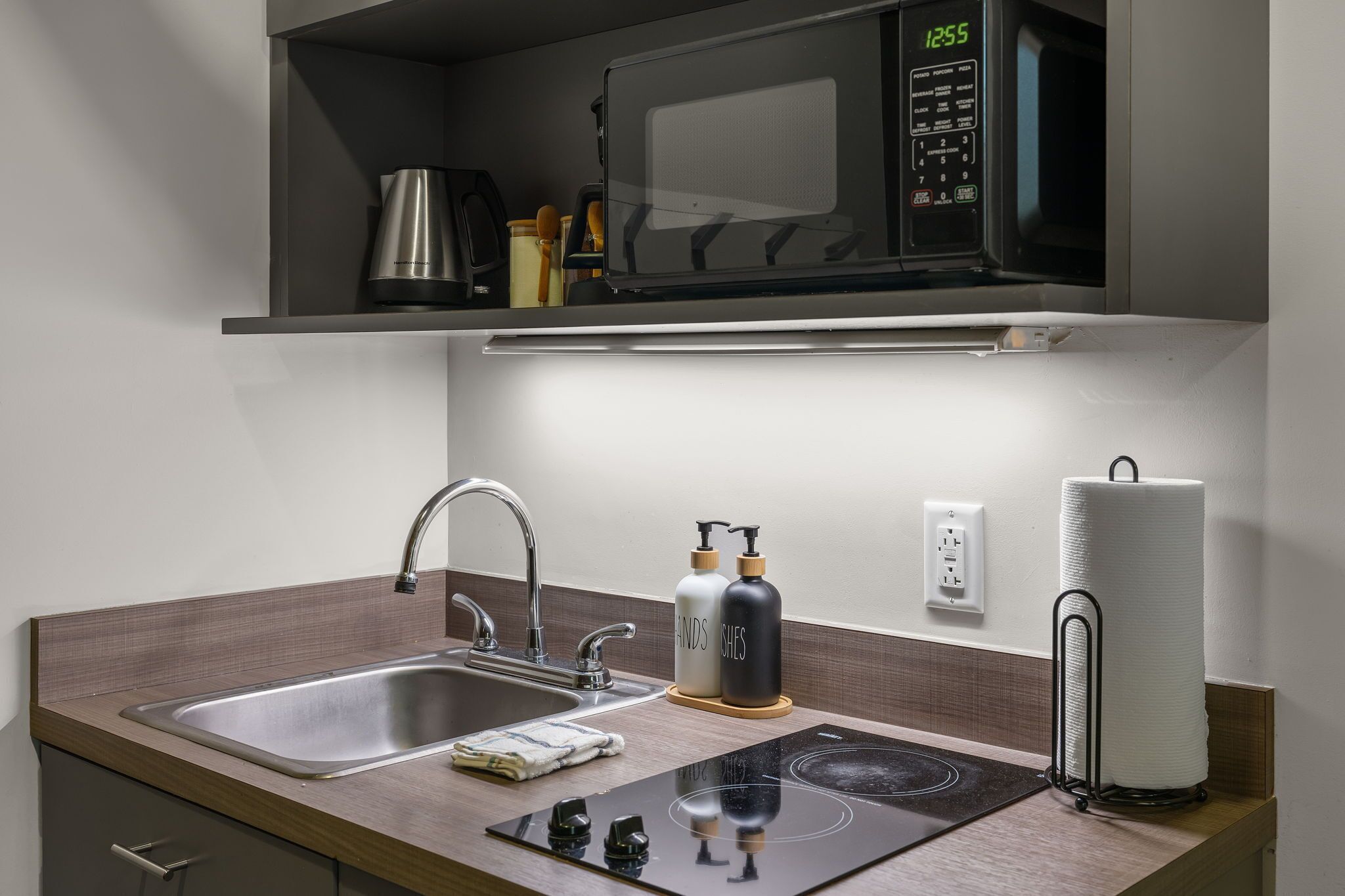 A modern kitchen with a built-in microwave, stainless steel sink, and a compact induction cooktop.