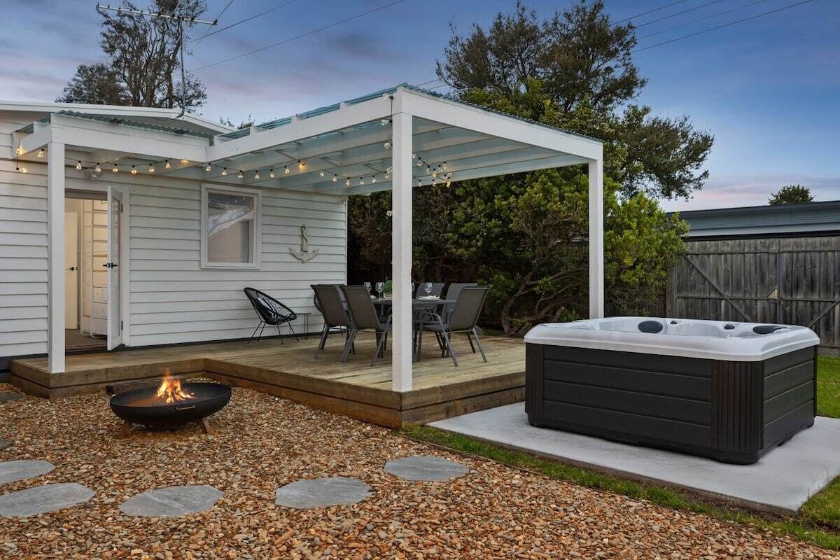 A covered patio with a fire pit, outdoor seating, and a hot tub.