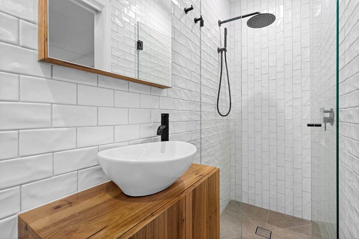 A modern bathroom with white subway tiles, a wooden vanity, a white vessel sink, a mirror, and a glass-enclosed shower area.