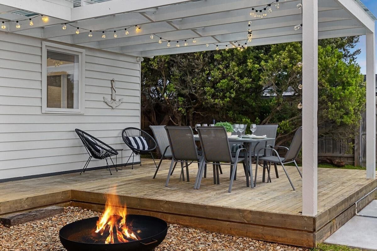 En overdækket terrasse med bålsted, udendørs møbler og lyskæder.