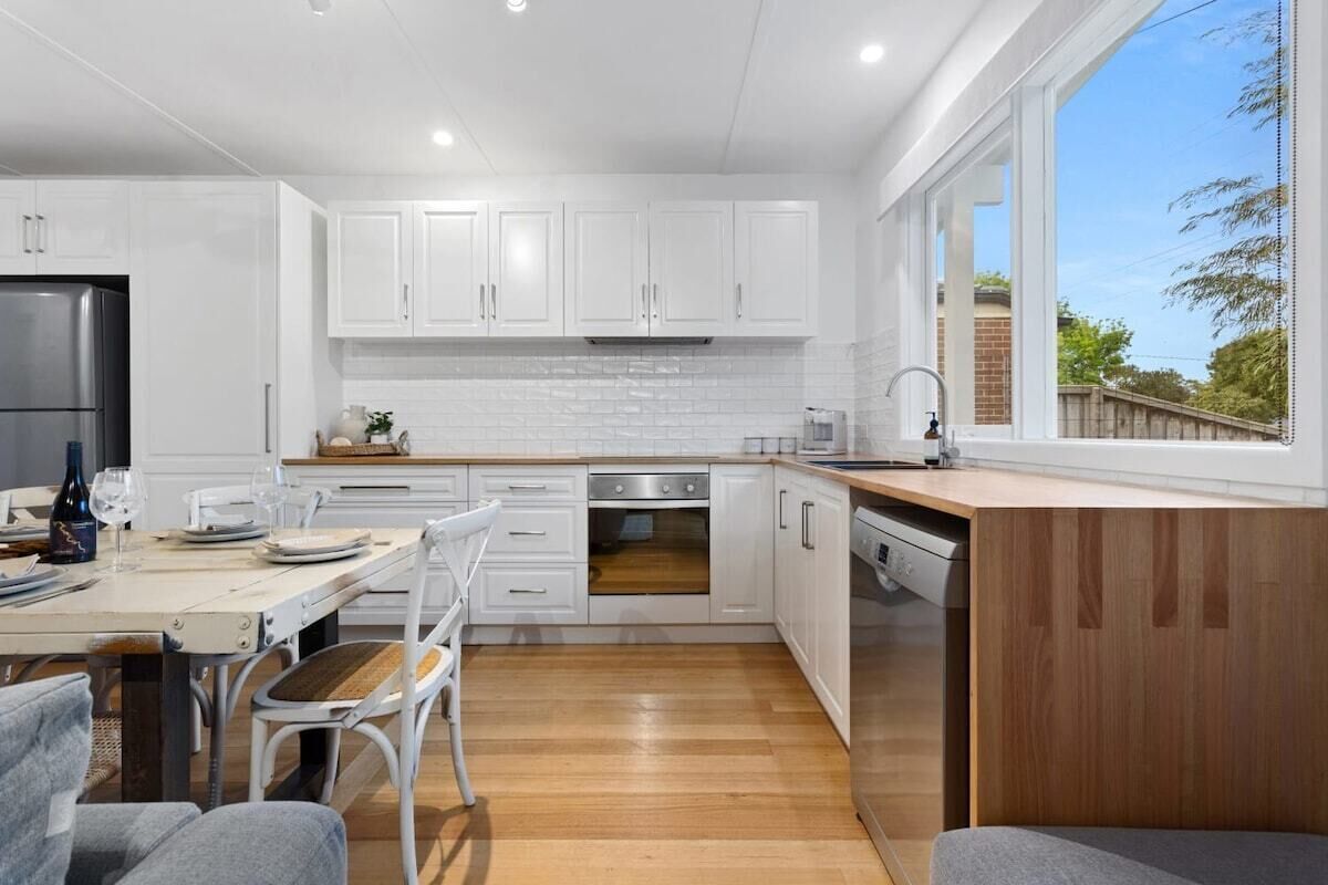 A modern kitchen with white cabinets, a stainless steel refrigerator, and a wooden dining table.
