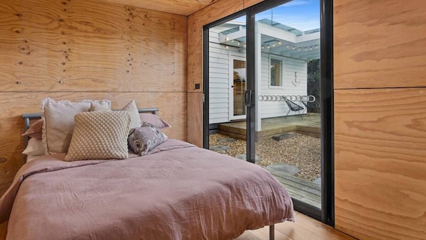Ein Schlafzimmer mit einem Bett, Kissen und einer Glastür, die zu einem Außenbereich mit Stuhl und Tisch führt.