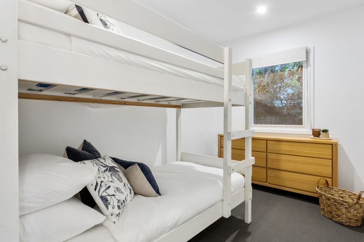 Une chambre avec un lit superposé, une commode en bois et une fenêtre donnant sur des arbres.
