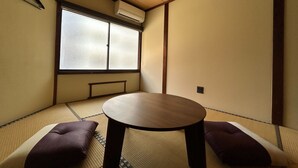 Una habitación tradicional japonesa con tatamis, una mesa baja, cojines, un divisor corredizo shoji y un equipo de aire acondicionado.