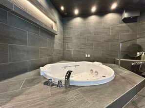 Un baño moderno con una bañera independiente, baldosas de piedra oscura e iluminación empotrada.