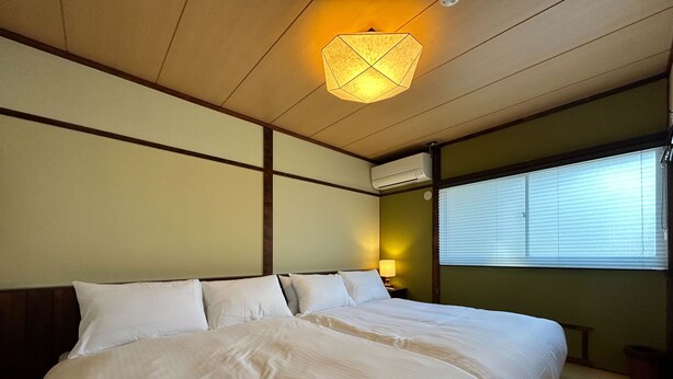 Habitación de hotel con una cama grande, una lámpara de noche, una lámpara de techo y una ventana con persianas.