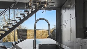 A modern kitchen with a marble countertop, stainless steel cabinets, and a unique staircase design.