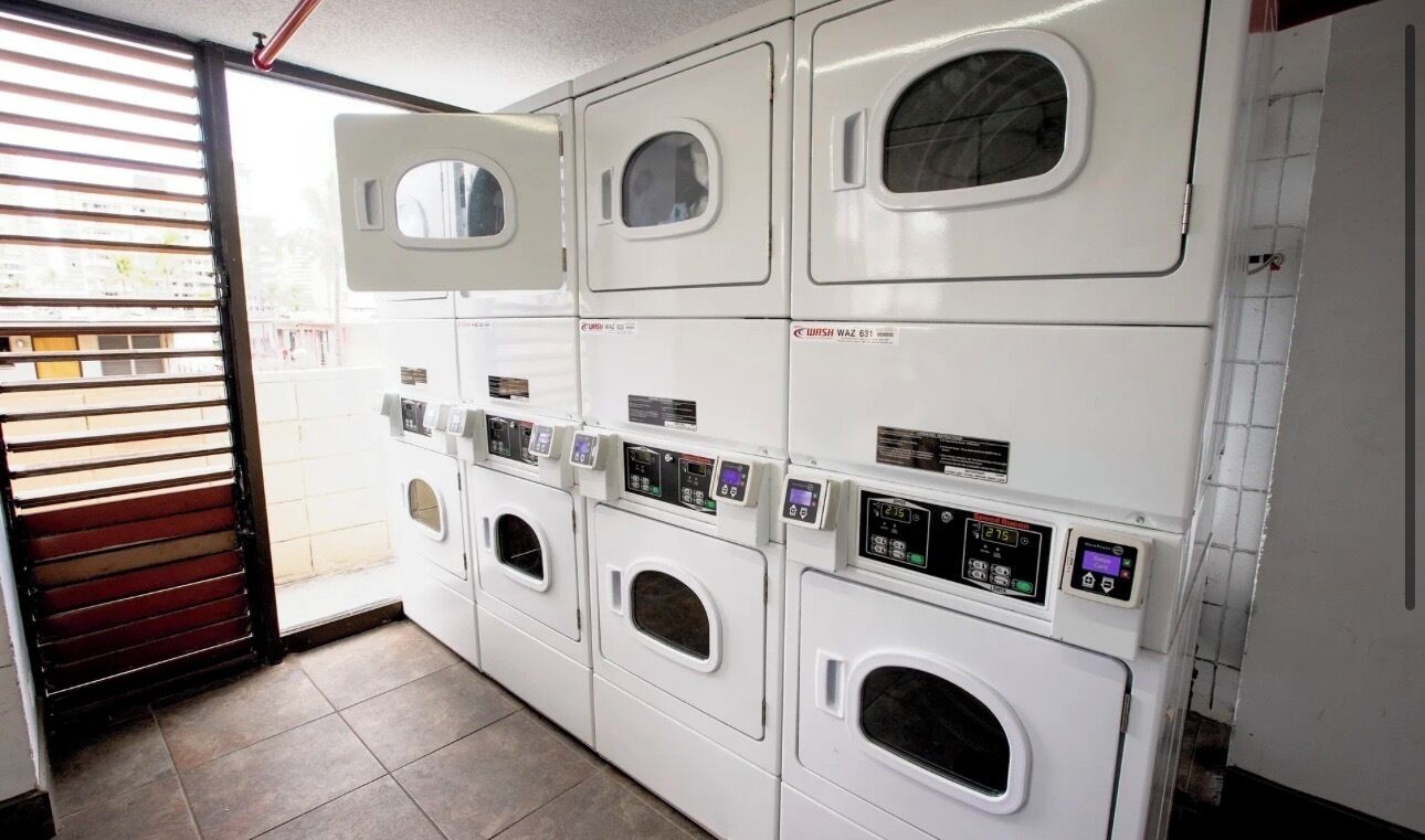 A row of white, modern, front-loading washing machines with digital displays, arranged in a commercial laundry facility.