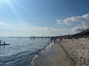 A beach with people walking and swimming, tents set up, and a pier in the background. - Lovely holiday home with garden near water (Rødby)
