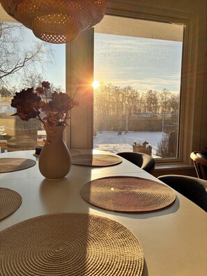 A dining table with placemats, a vase with flowers, and a view of a snowy landscape through a window. - Lovely holiday home with garden near water (Rødby)