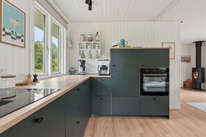 A modern kitchen with a built-in oven, a coffee machine, and a view of the outdoors. - Lovely holiday home with garden near water (Rødby)