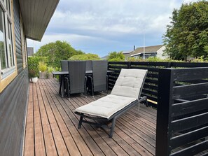 Une terrasse en bois avec une chaise longue, une table et des chaises.
