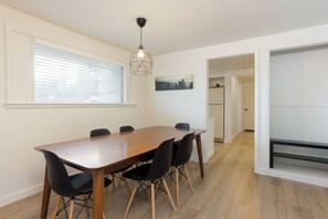 A dining area with a wooden table and black chairs, a hanging light fixture, and a window with blinds. - Best Location in Town! Walkable Westside 3BR (Bend)