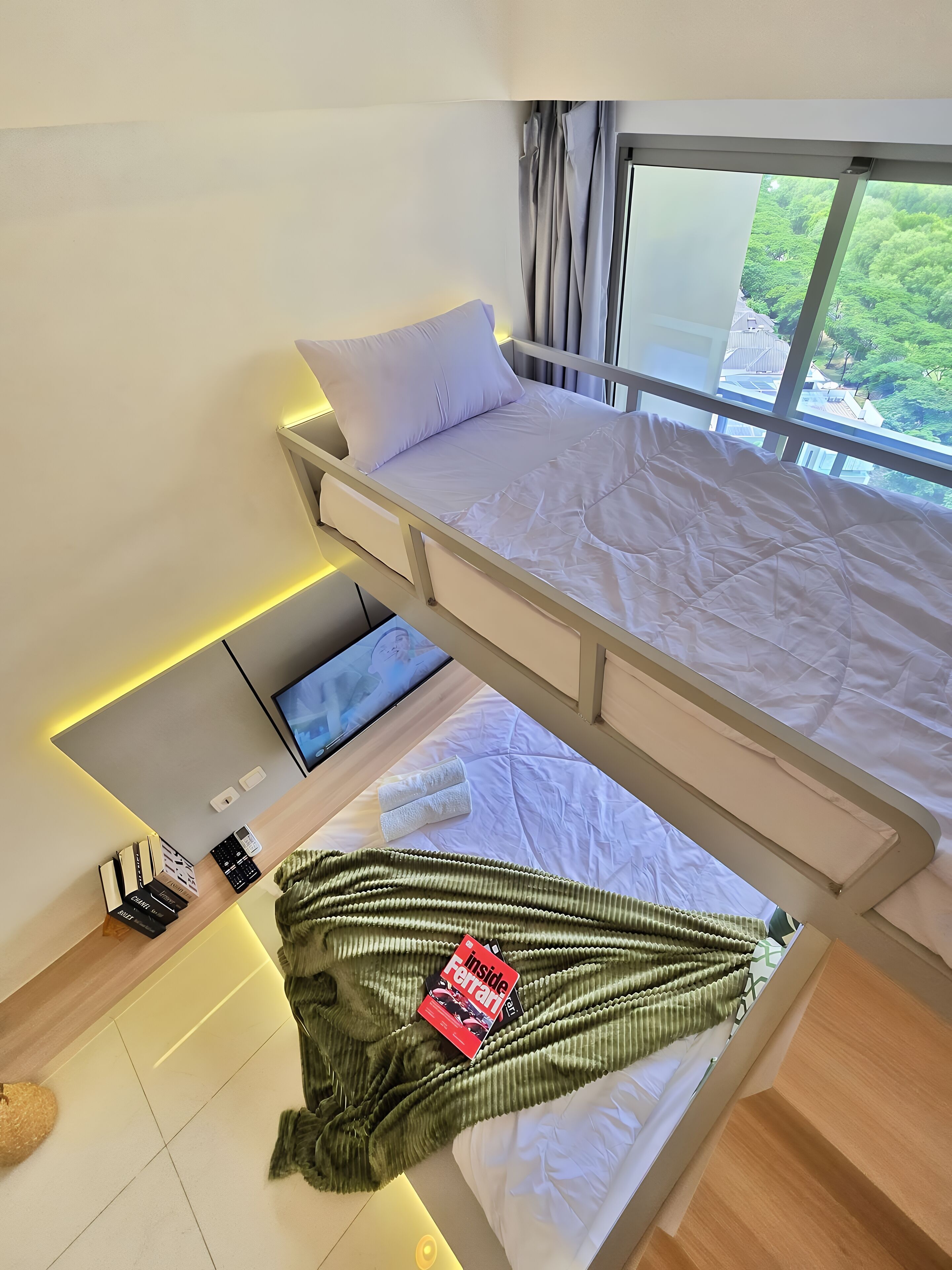Een moderne slaapkamer met een stapelbed, een bureau met een laptop, en uitzicht op groen.