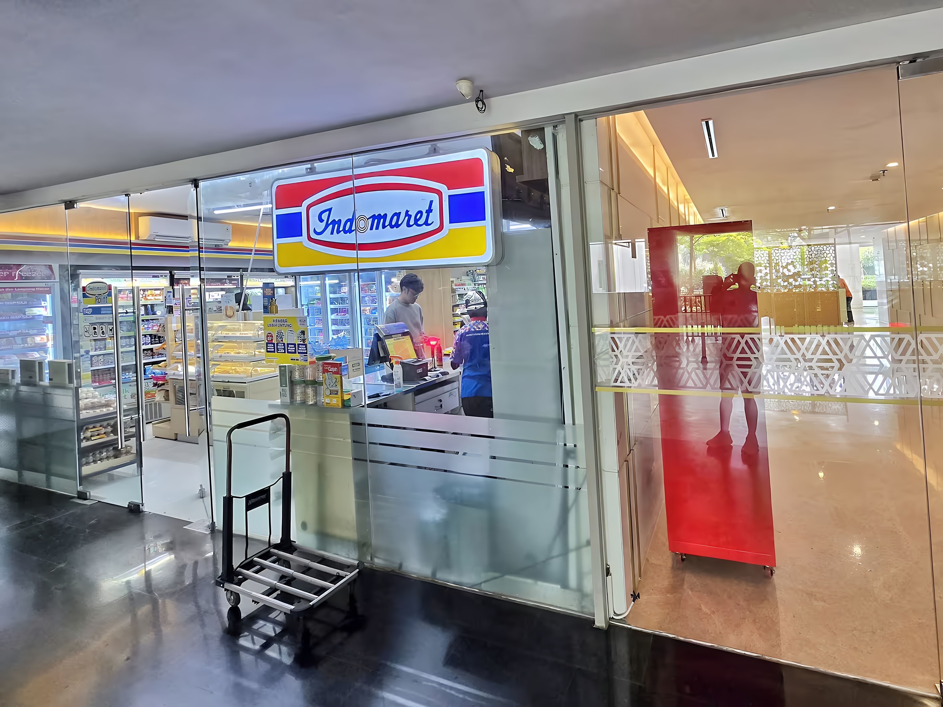 A store named Indomaret with a glass facade, a visible cashier, and a refrigerated display.