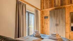 Quarto com guarda-roupa de madeira, cama com toalhas e janela com cortinas.