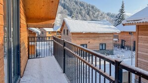 Uma cabana de madeira com varanda, telhados cobertos de neve e montanhas ao fundo.
