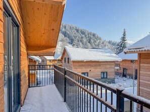 Une cabane en bois dotée d’un balcon, avec des toits recouverts de neige et un paysage montagneux en arrière-plan.