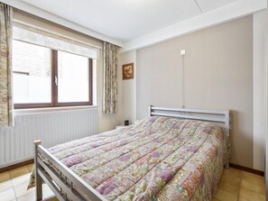 A bedroom with a bed, a window with curtains, a radiator, and a wall-mounted light fixture. - Pretty apartment on the casino (Blankenberge)